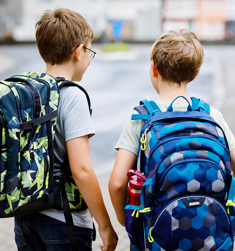 Zwei Jungs mit grünen und blauen Schulranzen gehen nebeneinander auf dem Weg zur Schule.