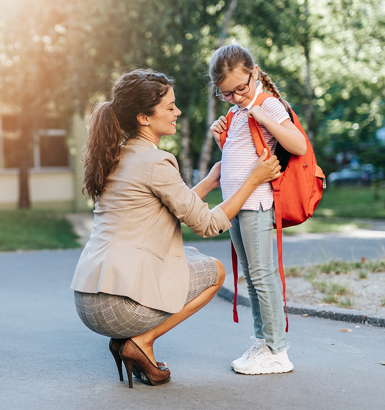 Mutter kniet vor Tochter und richtet den Sitz ihres Schulranzens.
