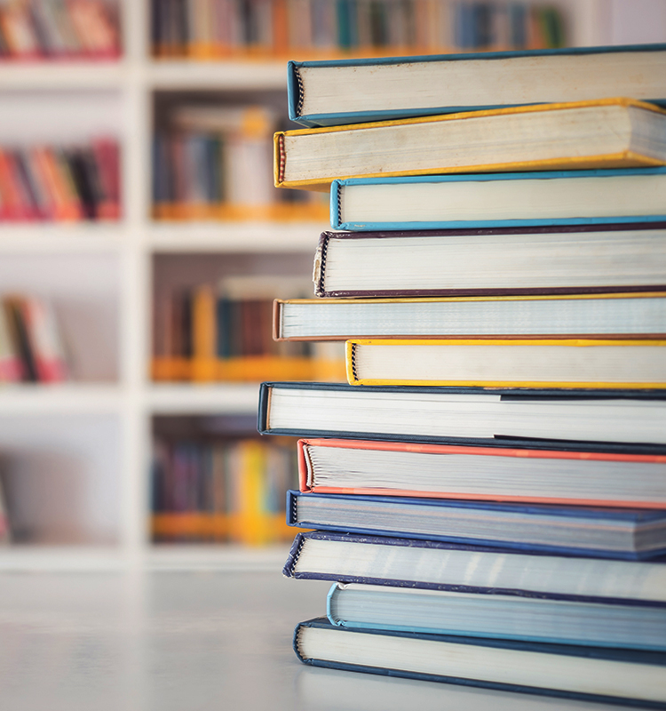 Mehrere Schulbücher liegen gestapelt auf einem Tisch. Im Hintergrund ist ein Bücherregal zu sehen.